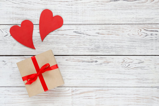 Kraft box with two red hearts on white wooden background.