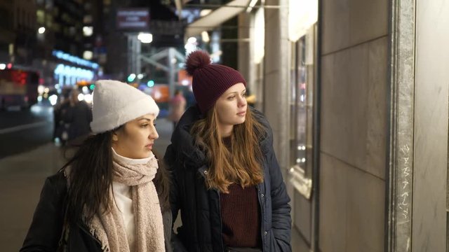 Two girls on a shopping trip in New York walk along shop windows