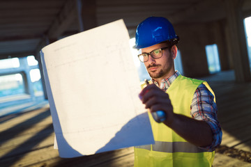 Male young architect with blueprints using walkie-talkie