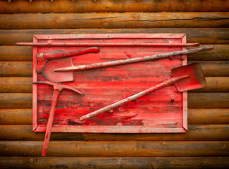 Red fire shield with axes and shovels  on a wooden wall of a bathhouse, Karelia, Russia