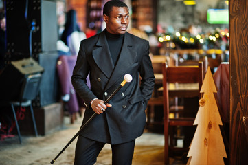 Stylish african american gentleman in elegant black jacket, holding retro walking stick as cane...