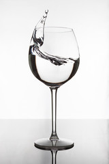Transparent wine glass with frozen splash of water. The glass stands on a black mirror surface on which its reflection is visible. The background is white.
