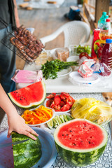 Women's hands cut with a knife into slices of ripe watermelon
