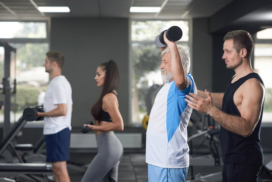 Elderler Serious Man Training In Crowded Gym.