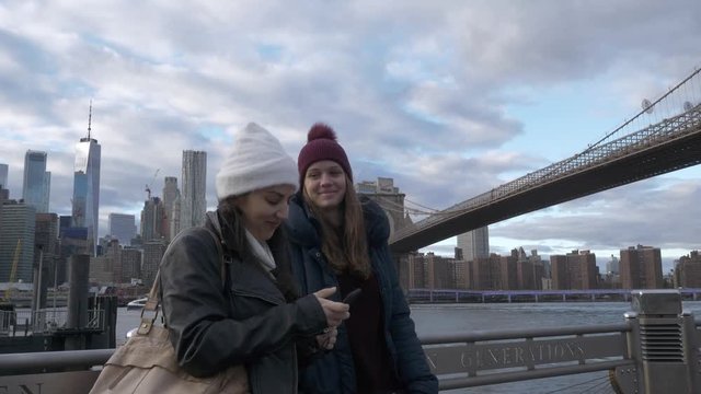 Two young women in New York walk along the typical skyline at Brooklyn Bridge