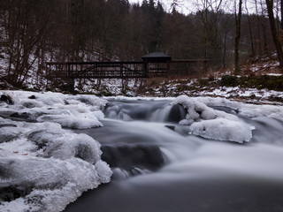 Fototapeta na wymiar smooth motion of wild water in a river in winter with snow and ice on rocks and stones in the beautiful nature of a forest