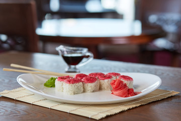 rolls with rice, red caviar, sesame, on a plate with wasabi, pickled ginge, chopsticks, nearby is soy sauce