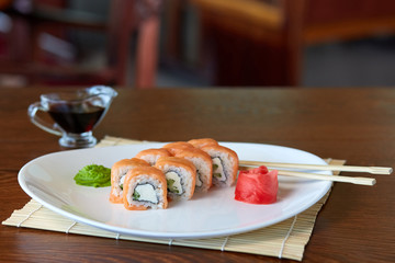 rolls with salmon, rice, nori algae, cream cheese and cucumber, lying on a white plate with wasabi and pickled ginger