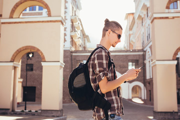 Side view - handsome hipster tourist guy with a backpack looks at the sights using the navigator and maps. Concept of tourism and convenience of orientation