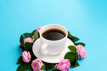 White cup with black coffee and pink roses lined around on a blue background