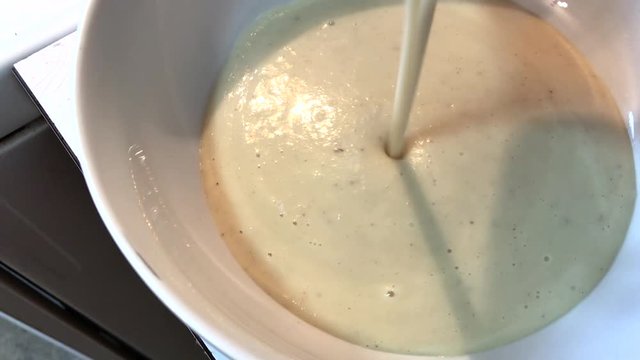 Delicious creamy white potato soup or celeriac soup is slowly being poured into a bowl