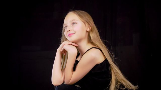 Portrait beautiful girl with long hair waving in wind on black background. Blond girl teenager posing on black background in dark studio. Fashion model concept. Locked shot