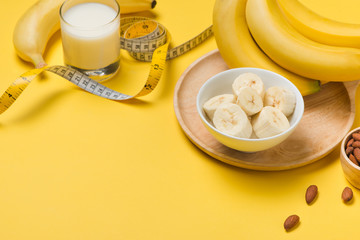 Measuring tape wrapped around a banana with almond on a yellow background, Concept of diet.