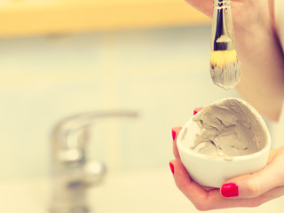 Female hand holding clay mud mask and brush. Skin care.