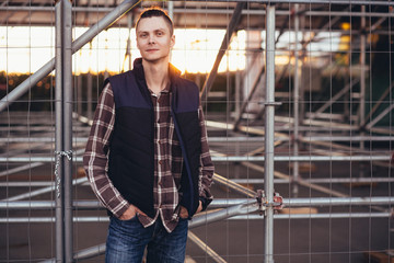 Fototapeta premium Cute young hipster guy posing against a background of barred building with iron structures. The concept of tourist walks around the city
