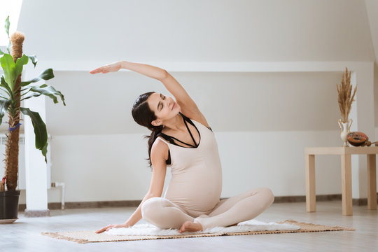 Pregnant woman stretching and training at home. Expectant female makes yoga exercise, healthy pregnancy concept