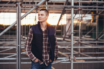 Fototapeta premium Cute young hipster guy posing against a background of barred building with iron structures. The concept of tourist walks around the city