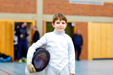 Little kid boy fencing on a fence competition. Child in white fencer uniform with mask and sabre....