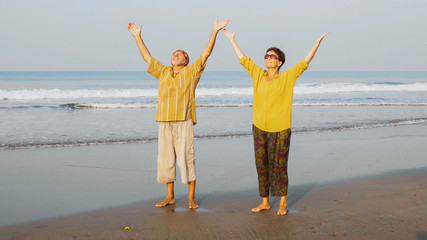 Aged couple practicing yoga on the beach.