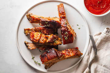 Bbq pork ribs with chili sauce on white plate. Pork ribs on slate background. Copy space.
