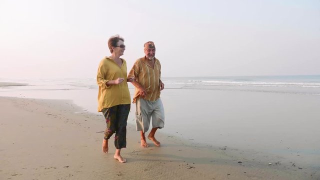 Active senior couple running on the sandy beach at sunrise