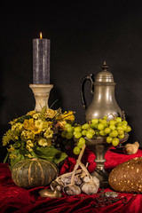 Dutch still life with grapes and candle and red draperies on a dark black background