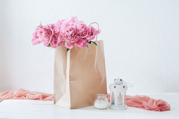 Pink peonies in a paper bag on a white table