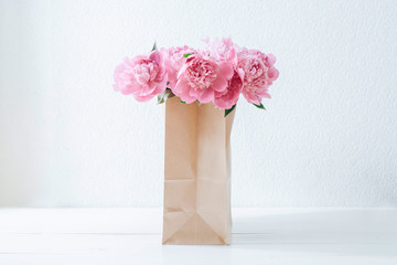 Pink peonies in a paper bag on a white table