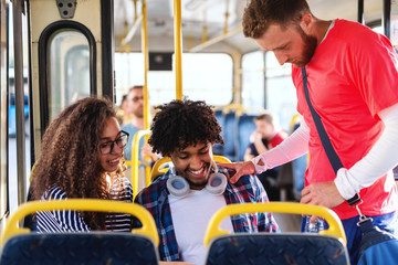 Small group of multicultural friends looking at tablet while driving in the city bus.