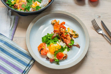 Fresh rustic breakfast - fried egg with bacon, onion and cherry tomatoes on a plate on a light wooden background
