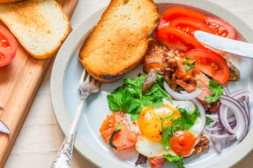 Fresh rustic breakfast - fried egg with bacon, onion and tomatoes on a plate  and toast on a light wooden background, close-up