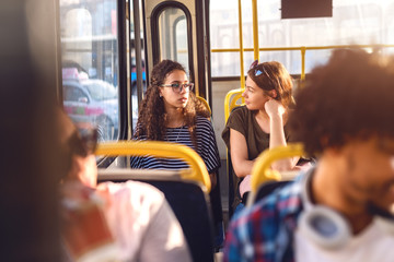 Two friends sitting in a bus, talking watching trough window.