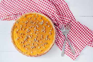 Homemade pumpkin pie on white plate with napkin and red flowers