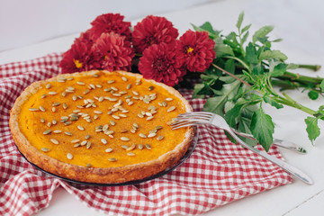 Homemade pumpkin pie on white plate with napkin and red flowers