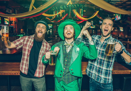 Happy and positive young people stand together and sing. They excited. Guy in middle wear St. Patrick's suit.