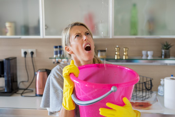 Shocked woman holding bucket for leaking water at home