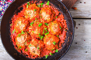 Meatballs in tomato sauce garlic and parsley in an iron frying pan on a white wooden background. Top view. Copy space