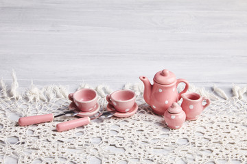 Pink tiny dotted ceramic utensils on the white rusty wooden table. Tea cups, a teapot, spoons and...