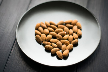 image of almond in the black plate. Nuts. Shape of heart. Love. Heart on a plate.
