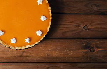 Fresh homemade pumpkin pie with cream on dark rustic wooden background.