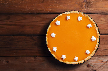Fresh homemade pumpkin pie with cream on dark rustic wooden background.