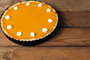 Fresh homemade pumpkin pie with cream on dark rustic wooden background.