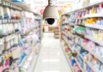 Modern White Dome CCTV camera on a ceiling on blurred supermarket department store background....