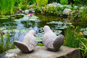 A couple of birds - garden sculpture against a pond 