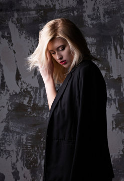 Stunning blonde woman wearing jacket and bra posing at studio with shadows
