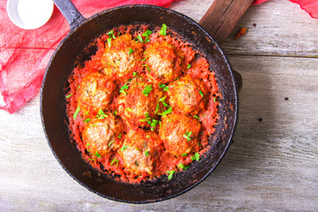 Meatballs in tomato sauce garlic and parsley in an iron frying pan on a white wooden background. Top view. Copy space