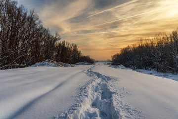 Path in the snow showing footsteps in winter time in sunset, low temperature, in the forest