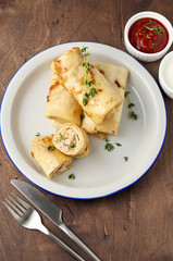 Savory crepe rolls with ground meat filling served with sour cream and tomato sauce