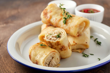 Savory crepe rolls with ground meat filling served with sour cream and tomato sauce