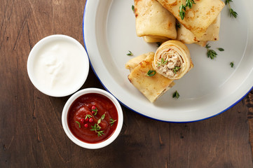 Savory crepe rolls with ground meat filling served with sour cream and tomato sauce